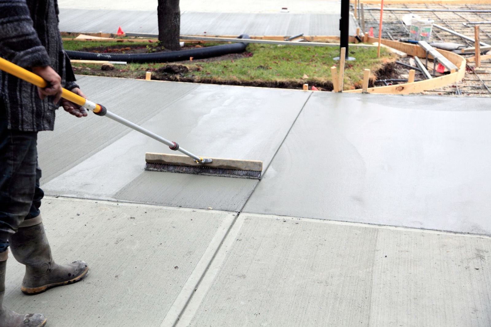 Worker applying a broom finish to a fresh concrete surface